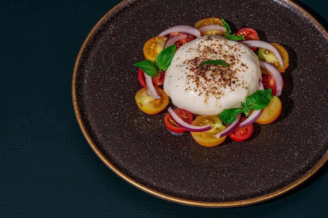 Burrata com tomate e manjericão, vista de cima, num prato escuro