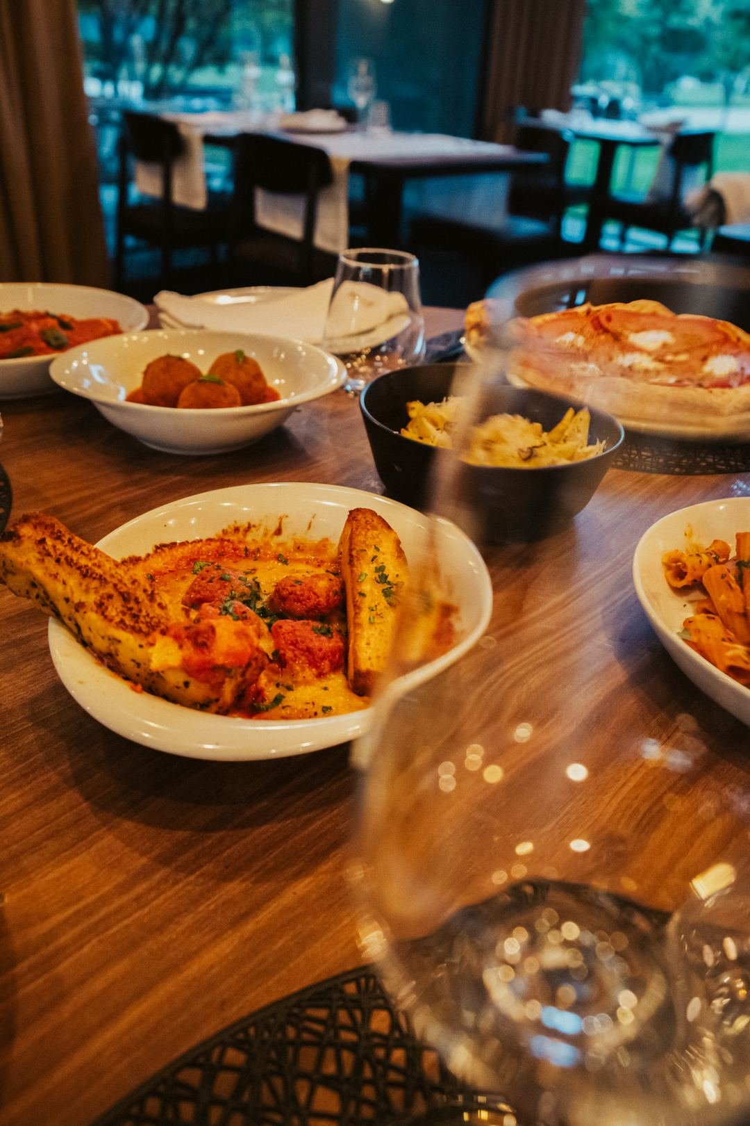 Uma mesa de grupo com pratos de massa, pão e queijos para partilhar